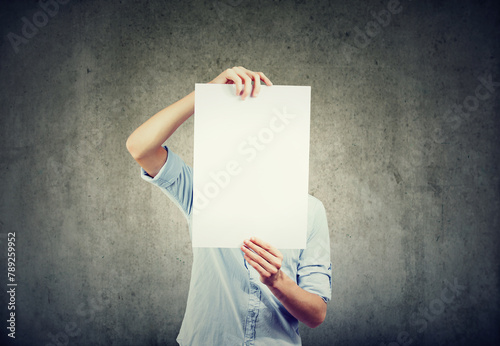 A young man holds a sheet of white paper in front of his face