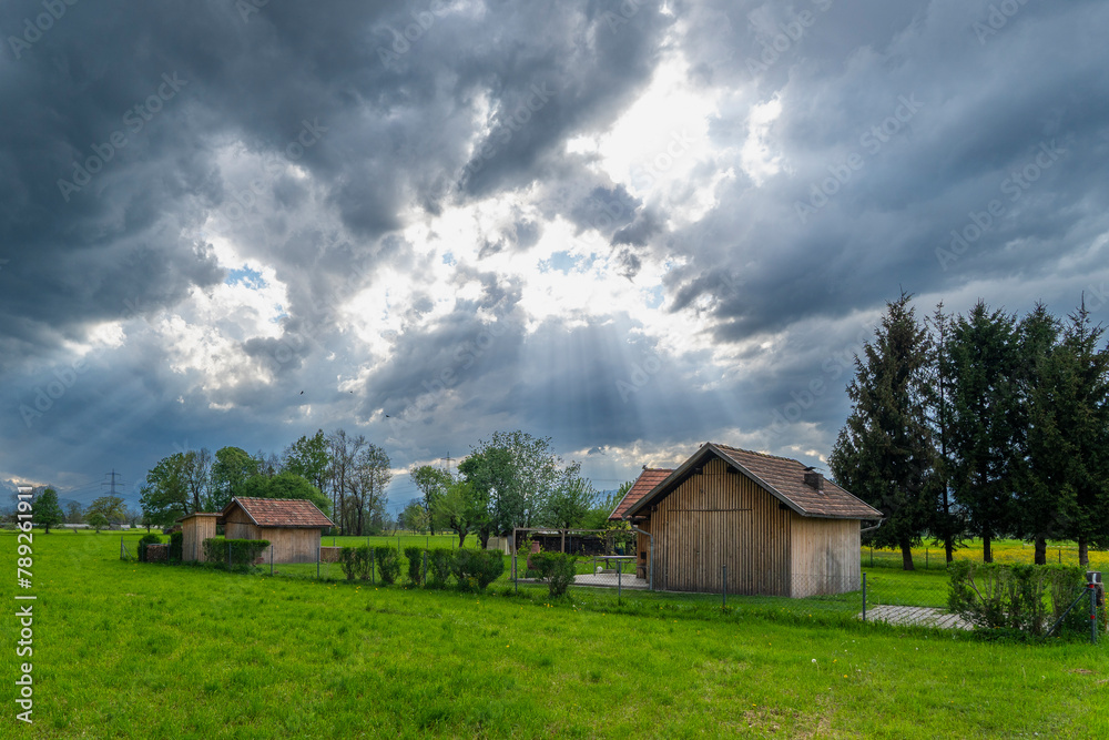 sun rays through the clouds, impressive weather atmosphere, next to a barn stands a tree, the single linden tree is dominant and towers over the hut. Dornbirn, Vorarlberg sun rays through the clouds, impressive weather atmosphere, next to a barn stands a tree, the single linden tree is dominant and towers over the hut. Dornbirn, Vorarlberg