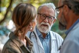 Elderly doctor in conversation with two people outdoors, looking concerned
