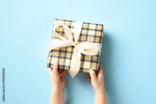 Child's hands holding gift box over pastel blue background.