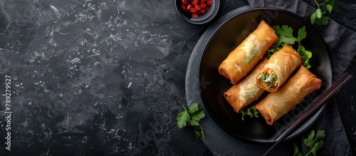 Top view of fried spring rolls on a black iron plate against a grey stone slate background with space for text.