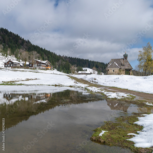 panorama with alpine wooden farmhouse named "Hämmerles Alp" in Bregenz forest, Vorarlberg, wonderful view in spring when the snow melts with a holiday home, pond and chapel on the snowy meadow