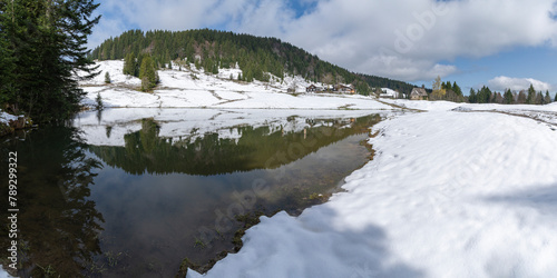 panorama with alpine wooden farmhouse named "Hämmerles Alp" in Bregenz forest, Vorarlberg, wonderful view in spring when the snow melts with a holiday home, pond and chapel on the snowy meadow