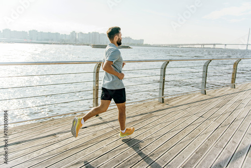 A man runs purposefully on a boardwalk, with a sunlit river glistening and a distant bridge connecting urban horizons.