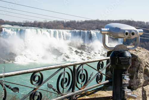 A closeup of coin operated viewing binoculars pointing at the Canadian Horseshoe Falls out of focus in the distance. Observation binoculars close-up with a view of the river and the city. High quality