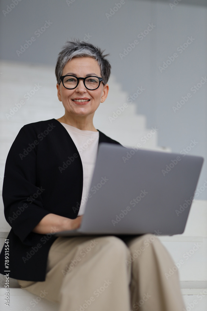 An entrepreneurial mature woman engages in online business from her modern office, blending technology with success. An entrepreneurial mature woman engages in online business from her modern office, blending technology with success.
