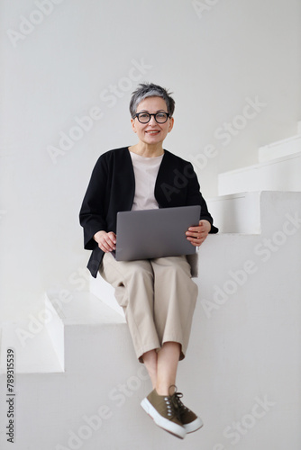 A mature pensioner woman embraces technology, working online with professionalism and joy from her home.