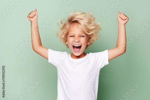 A little boy rejoices with his hands up in the air on a green solid background. photo