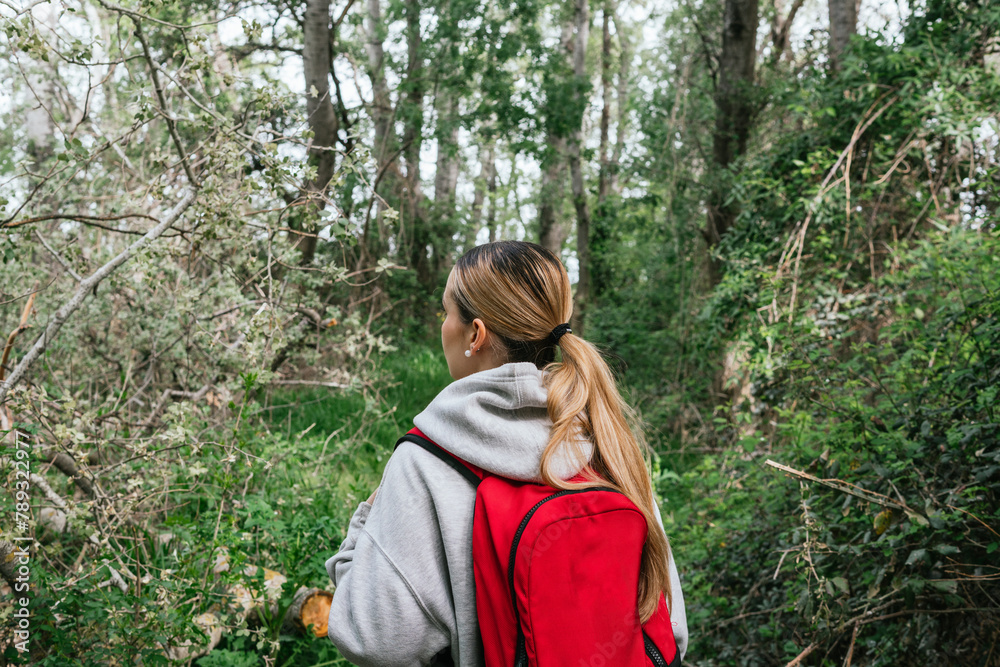 Woman seen from behind walks along a natural path full of vegetation and trees Woman seen from behind walks along a natural path full of vegetation and trees