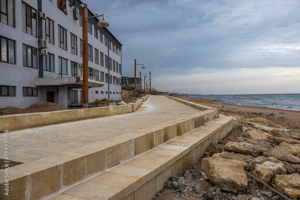 Construction of an embankment by the sea. Landscaping of the coastal area. Buildings near the shore. The embankment is made of blocks of natural hewn stone.