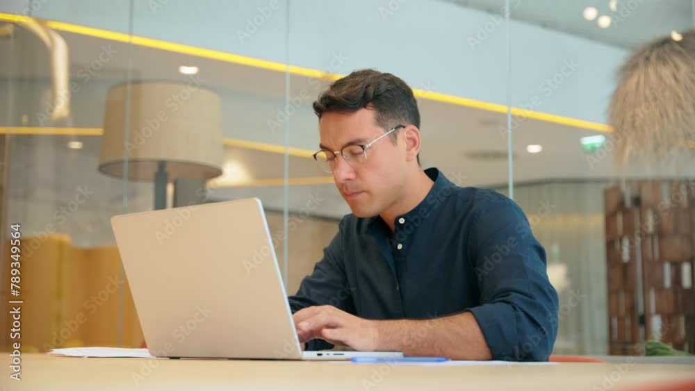 Busy professional business man executive, young male corporate employee, latin businessman wearing eyeglasses typing on computer technology using laptop searching on web working at office desk.
