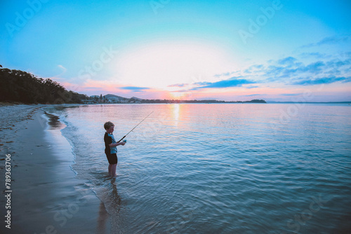 Young boy fishing on the beach at sunset photo