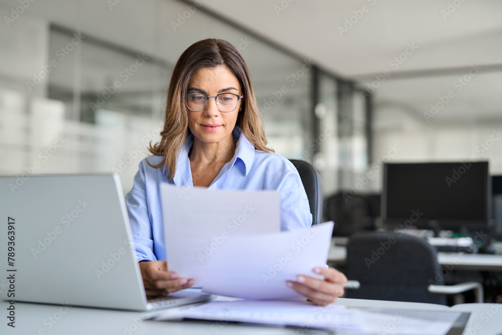 Naklejka premium Busy mature business woman entrepreneur working in office checking legal document account invoice in office. Businesswoman of middle age manager executive or lawyer using laptop computer at work.