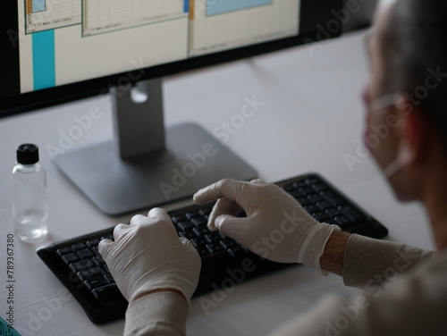 Young woman wearing protective gloves on hands and mask on face working from office or home using laptop on desk.