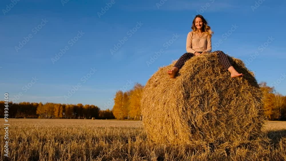 Laughing young woman throws shoes at the camera on haystacks. Pretty girl in casual clothes gets fun on farmer field Laughing young woman throws shoes at the camera on haystacks. Pretty girl in casual clothes gets fun on farmer field