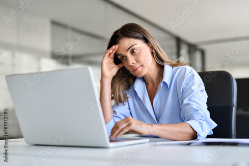 Worried fatigued mature business woman having headache at work. Tired upset busy 40s middle aged businesswoman feeling stress having problem at workplace looking at laptop computer in office. photo