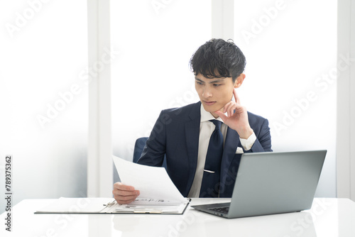 ノートパソコンと書類チェック作業する男性ビジネスマン