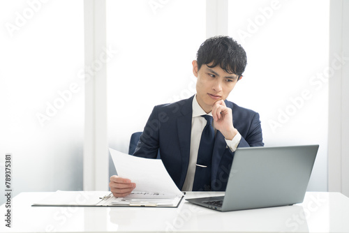 ノートパソコンと書類チェック作業する男性ビジネスマン