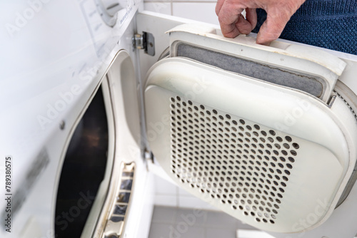 A man removes lint from an electric  clothes tumble dryer