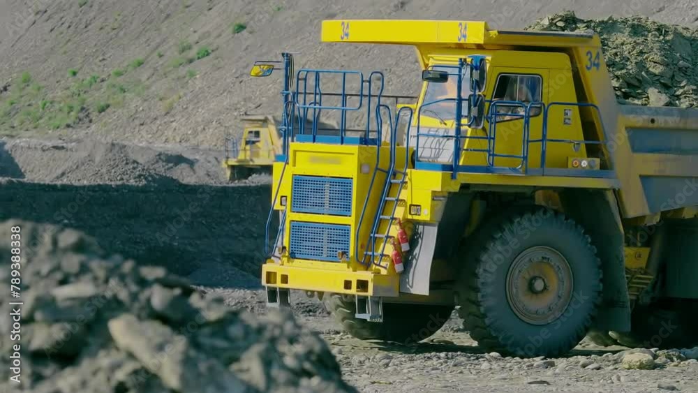 Heavy truck is transporting huge amount of rocks at the open-pit mine. Yellow heavy truck is fully loaded with rocks. Heavy truck is carrying the rocks in the box at the carrier. Mining Quarry. Heavy truck is transporting huge amount of rocks at the open-pit mine. Yellow heavy truck is fully loaded with rocks. Heavy truck is carrying the rocks in the box at the carrier. Mining Quarry.