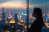 Asian Business Woman Looking Over the Evening City Lights From the Window of a High-Rise Building