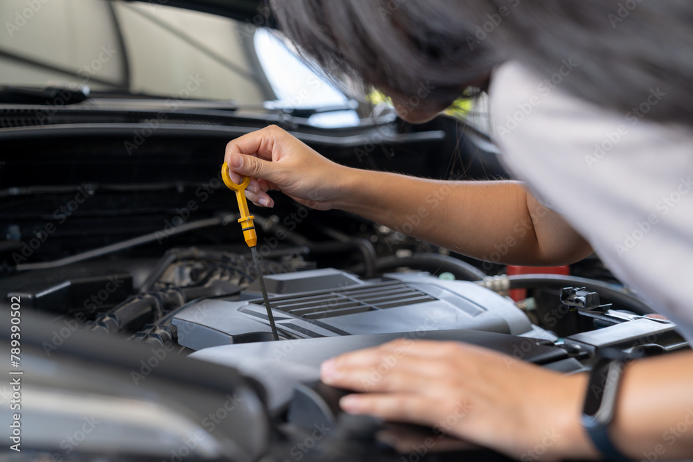 The woman is checking the engine oil of the car