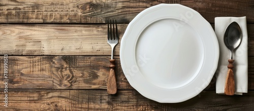 A white, vacant plate accompanied by utensils, set against a backdrop of wooden texture. photo