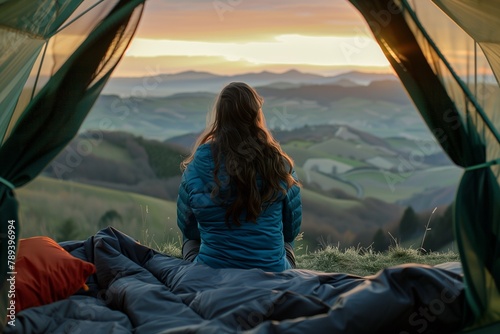 A woman is sitting in her tent at the top of an outdoor mountain, watching the sunrise over distant mountains while camping. using natural lighting, for the best photo rendering of cinematic lighting