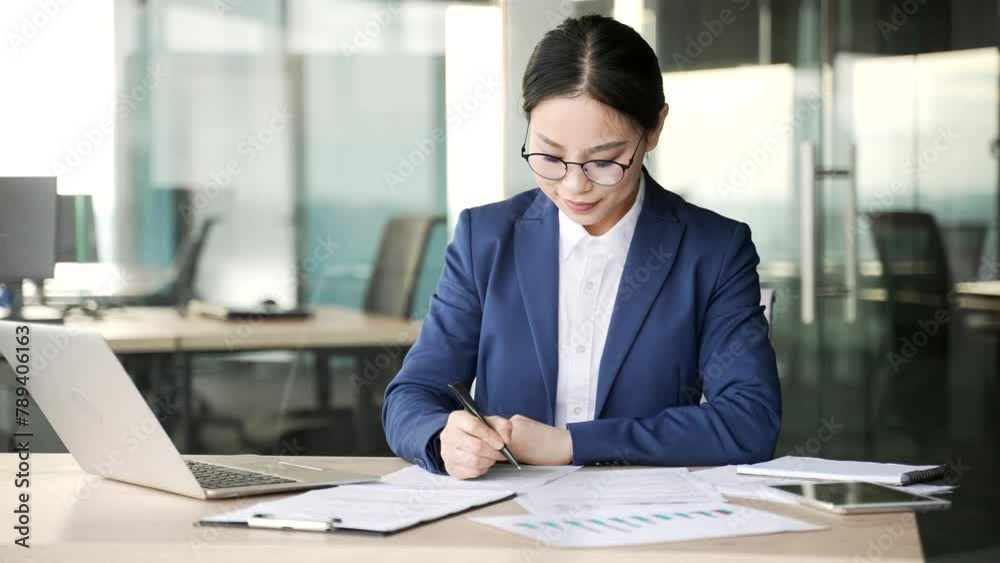 Busy young asian businesswoman fills out documents with pen sitting at workplace in business office. Woman entrepreneur or financier doing paperwork, making a financial report or writing tax form
