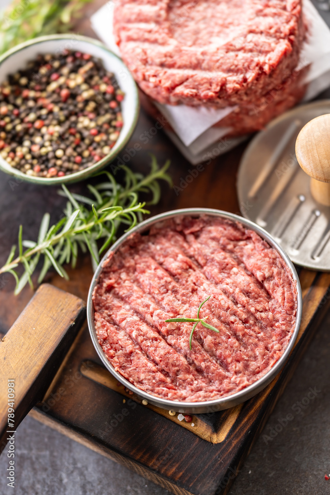 Fresh raw ground beef patties with rosemary salt and pepper made in a meat form on a cutting board Fresh raw ground beef patties with rosemary salt and pepper made in a meat form on a cutting board