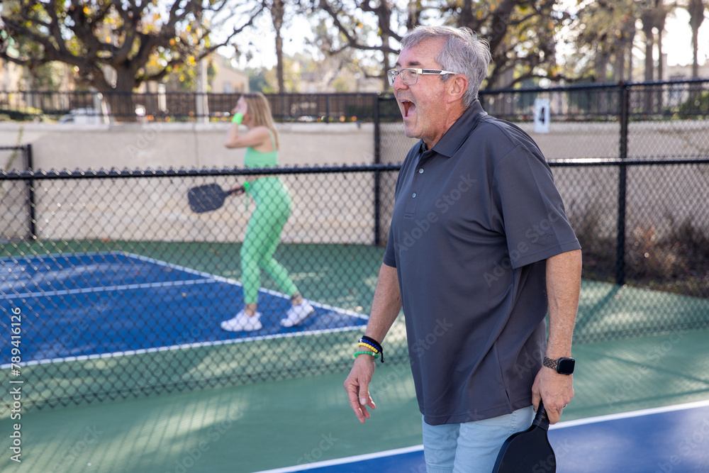 Mature pickleball having fun on the court during a game outside. The popular sport is great exercise for all ages. Mature pickleball having fun on the court during a game outside. The popular sport is great exercise for all ages.