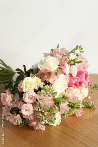Beautiful bouquet of fresh flowers on wooden table near white wall