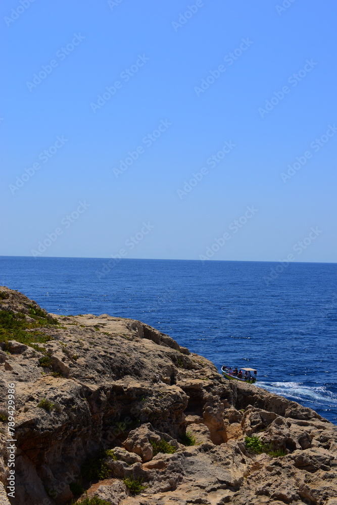 ZURRIEQ, MALTA - Augusts 06, 2021: The Blue Grotto - A famous sea cave surrounded by the deep blue sea at southern Malta. On a traditional boat surrounded by more brightly coloured boats. 