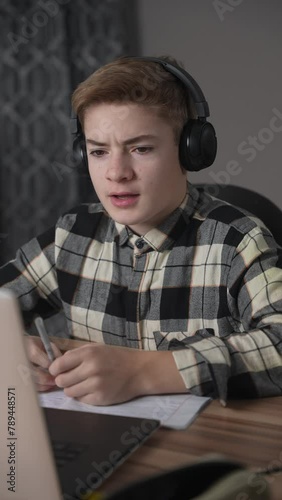 Adolescent schoolboy studying online using laptop at home. Smiling teenager looking to web camera and talking. Online education, distance learning concept, communication, conference call. Vertical