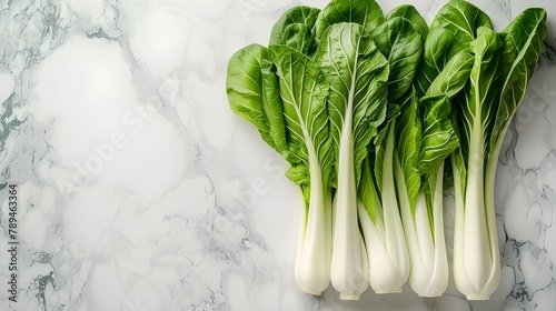 Heads of bok choy lie on the surface of white marble.