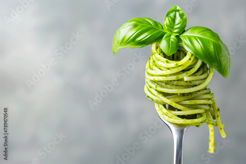 tasty italian spaghetti pasta with green pesto alla genovese and basil on a fork, closeup photo