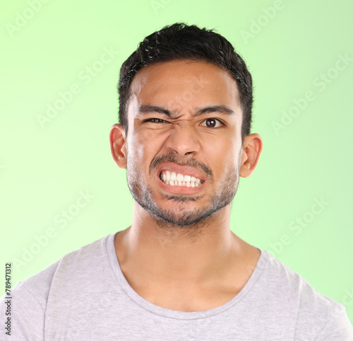 Man, portrait and angry face with disgust for awkward humor or funny humor on a green studio background. Frustrated male person or joker with goofy expression, attitude or upset behavior in anger