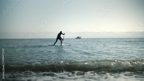 Man is floating on a surfboard, rowing with an oar. Male is doing paddleboarding or supboarding. Waves on the sea, surfing on the ocean. Hands pushing and pulling the paddle photo