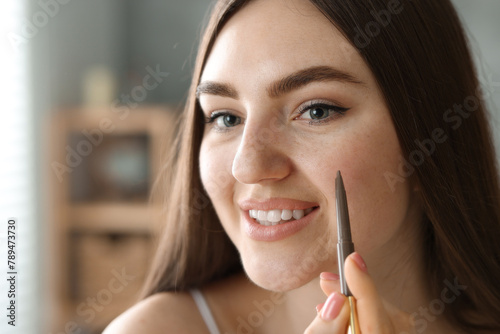 Smiling woman drawing freckles with pen indoors