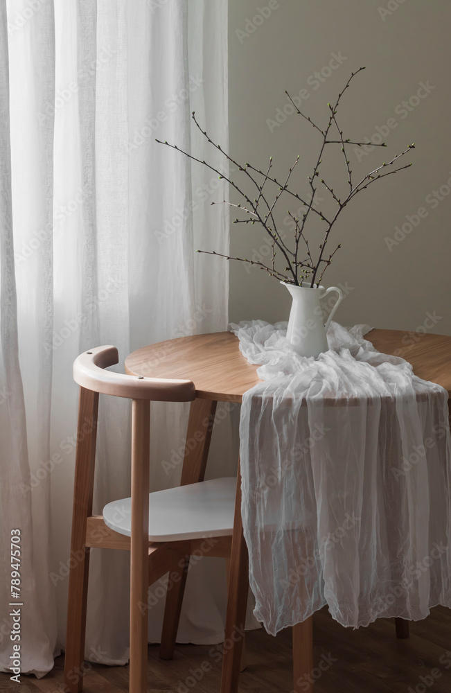 The simple interior of the living room - a round wooden table with a jug with branches and a chair. Minimalism style - obrazy, fototapety, plakaty 