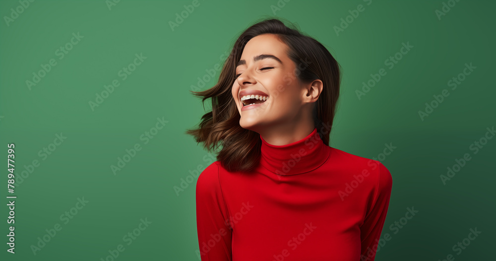 Fototapeta premium A vibrant image capturing a woman in a red turtleneck, eyes closed in a moment of genuine laughter, exuding warmth and happiness against a green background.