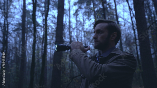 Detective looks for evidence in a rainy forest with a flashlight in hand, conducting an investigation 