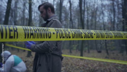 View of forensics experts and a detective working behind crime scene tape during an investigation 