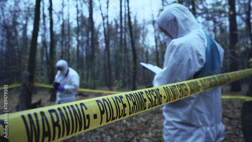 Forensic analysts work at a crime scene secured by tape, focusing on evidence collection 