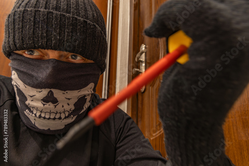 Burglary, a masked thief in a balaclava opens the door © macherstudio.pl
