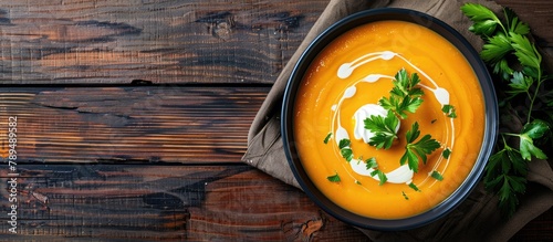 Top view copy space of pumpkin and carrot soup with cream and parsley displayed on a dark wooden background.