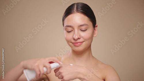 Funny happy attractive young woman applies skin care cream to her face, looks at the camera, applies moisturizing facelift cream. Slow motion