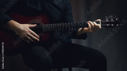 A man in a black shirt plays an acoustic guitar