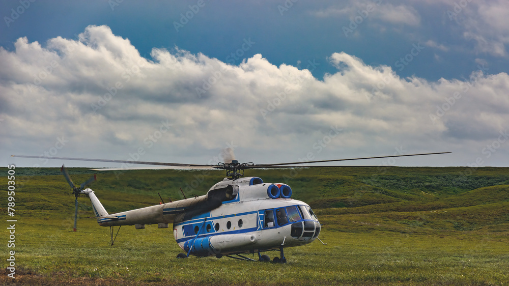 An Mi-8 passenger helicopter made an emergency landing in the northern summer tundra. Beautiful cloudy sky on the horizon. Green grass An Mi-8 passenger helicopter made an emergency landing in the northern summer tundra. Beautiful cloudy sky on the horizon. Green grass