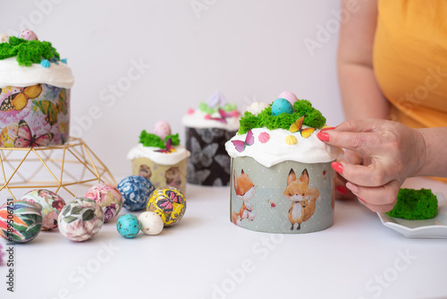 Chef's hands decoration of easter cake green cream and small colored chocolate eggs and colorful eggs on light background. Spring Christian holiday of Orthodox believers. 